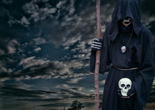 Grim reaper holds a skull in his hand, on a dark night sky.