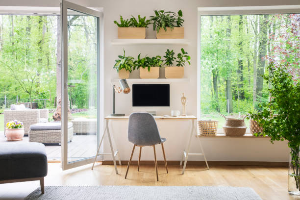 istock Inspirational workspace interior for a freelancer with computer on a wooden desk, white walls and the view of nature in the backyard outside 1016510130