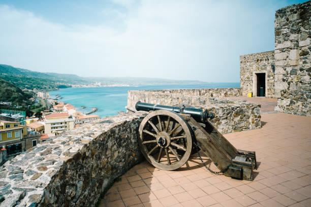 Medieval cannon on a remains of the ancient fortress on a background of the stone pine and other Mediterranean vegetation, sea and cloudy sky in overcast morning, Bordighera, Italy,