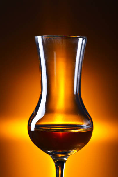 A high-angle artistic shot showing the hourglass-shaped light refraction cast by a glass of red tea on a white surface, illuminated by strong directional sunlight