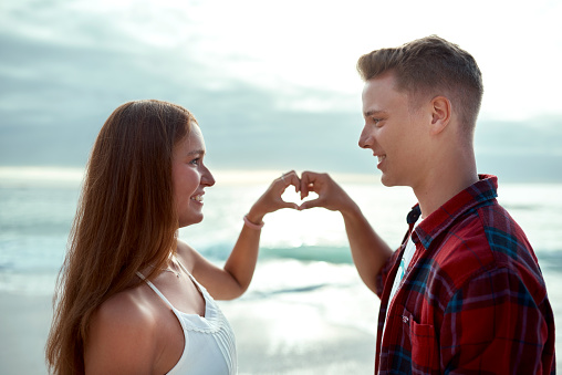 Shot of a happy young couple making a heart shaped gesture with their hands at the beach