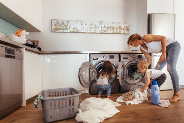 Family doing laundry together at home Woman with kids load clothes in washing machine. Mother and children putting laundry into washing machine at home. utility room stock pictures, royalty-free photos & images