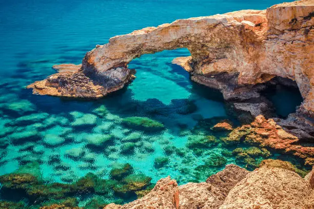 Photo of Beautiful natural rock arch near of Ayia Napa, Cavo Greco and Protaras on Cyprus island, Mediterranean Sea. Legendary bridge lovers. Amazing blue green sea and sunny day. Creative split toning