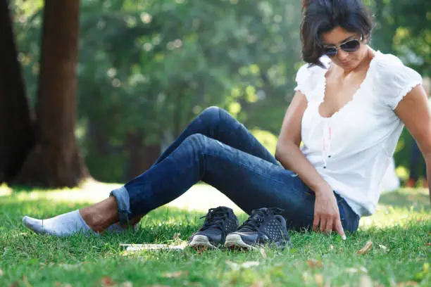 The girl took off her shoes and was resting barefoot on the grass in the park. Notepad and pencil - the concept of creative thinking and the search for new solutions.