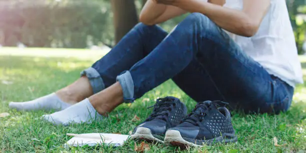 The girl took off her shoes and was resting barefoot on the grass in the park. There is a notebook and a pencil for creative thinking and searching for new solutions. Communicate in a mobile phone chat.