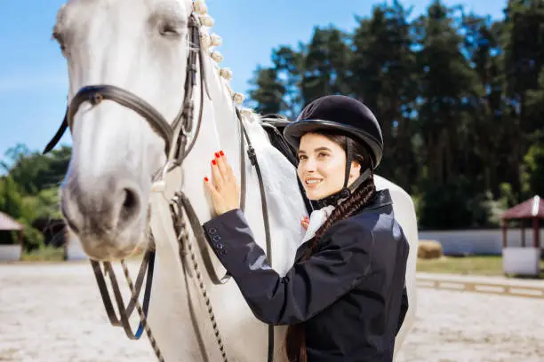 Fond of equestrianism. Beautiful beaming dark-haired woman with red nail art fond of equestrianism