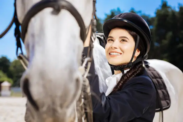 Excited woman. Dark-eyed beaming woman fond of equestrianism feeling excited before taking part in contest