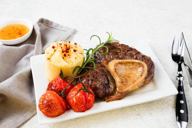 istock Prepared beef steak osso bucco with mashed potatoes and tomatoes on white table 1016541878