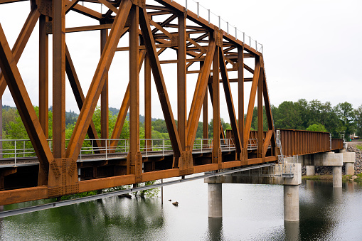 A new unpainted rusted metal truss railway bridge on concrete piles across the Washougal River in Camas Washington in national recreation Columbia Gorge area