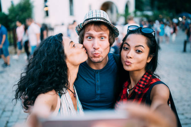 Friends taking selfie and giving a kiss Friends taking selfie on street and giving a kiss. three way kiss stock pictures, royalty-free photos & images