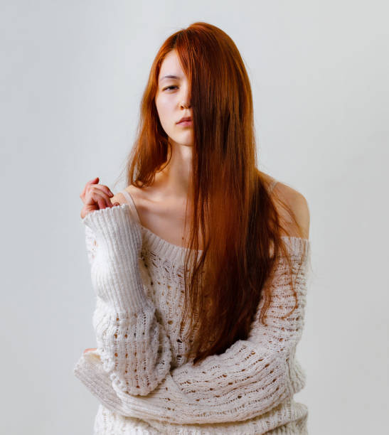 Portrait of young beautiful long red hair woman in knitted sweater and hair covering half of her face. Naked shoulder while posing on grey background copy space. Portrait of young beautiful long red hair woman in knitted sweater and hair covering half of her face. Naked shoulder while posing on grey background copy space. vogue cover stock pictures, royalty-free photos & images