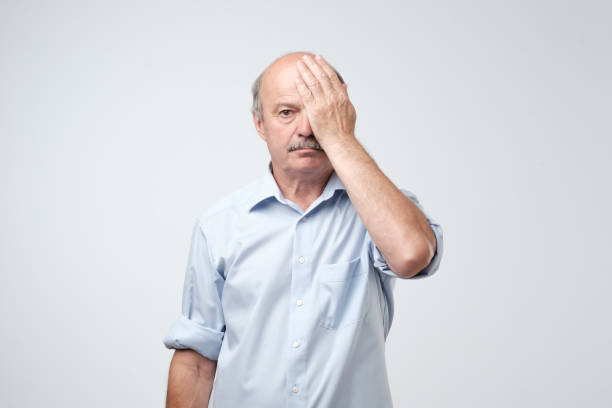 homme européen fatigué nature couvrant un œil avec palm, comme si avoir ses yeux testés au cours de l’examen de la vision - optics store photos et images de collection