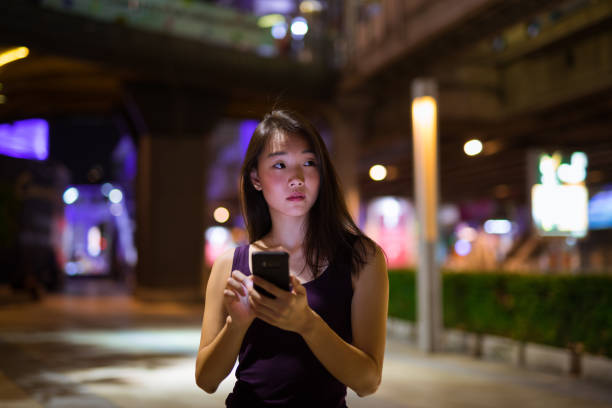 istock Beautiful Asian Woman Outdoors At Night Using Mobile Phone 1016585502