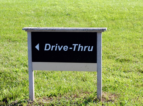 A small brown wood drive thru sign in the grass.