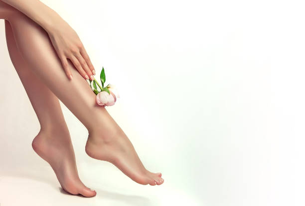 mano de mujer agraciada es flor de peonía y tocar pies bien arreglados. detalles de primer plano del cuerpo humano - human leg smooth human skin human foot fotografías e imágenes de stock