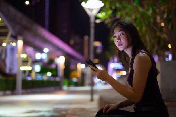 istock Beautiful Asian Woman Outdoors At Night Using Mobile Phone 1016591916