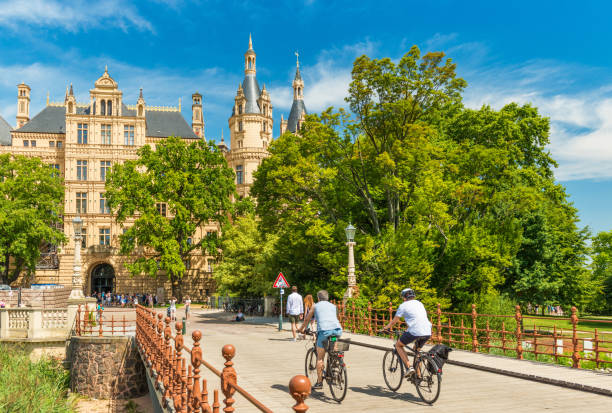 Schwerin, Germany: Two cyclists moving towards the Schwerin Castle, the most famous landmark of the state of Mecklenburg-Vorpommern Schwerin - July 2018, Germany: Two cyclists moving towards the Schwerin Castle, the most famous landmark of the state of Mecklenburg-Vorpommern schwerin castle stock pictures, royalty-free photos & images