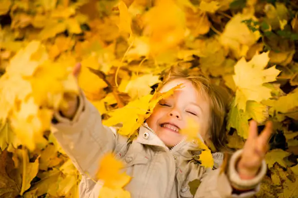 Little child lying in ground and catching falling leaves in autumn