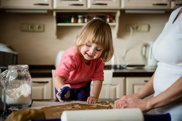 Mother and child cutting out cookies from dough at home kitchen
