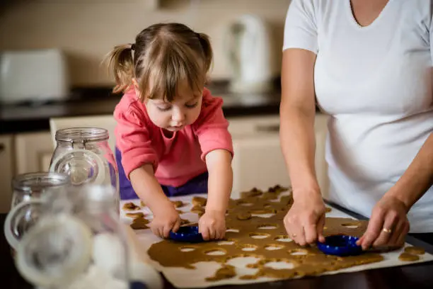 Mother and child cutting out cookies from dough at home kitchen