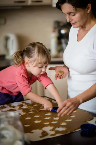 Mother and child cutting out cookies from dough at home kitchen