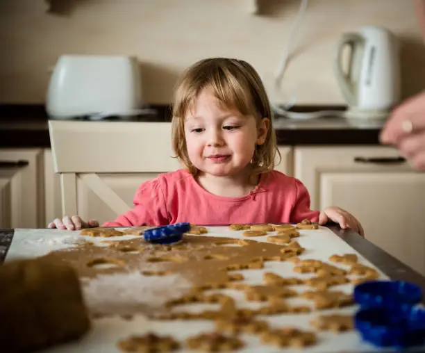 Child cutting out cookies from dough in kitchen at home
