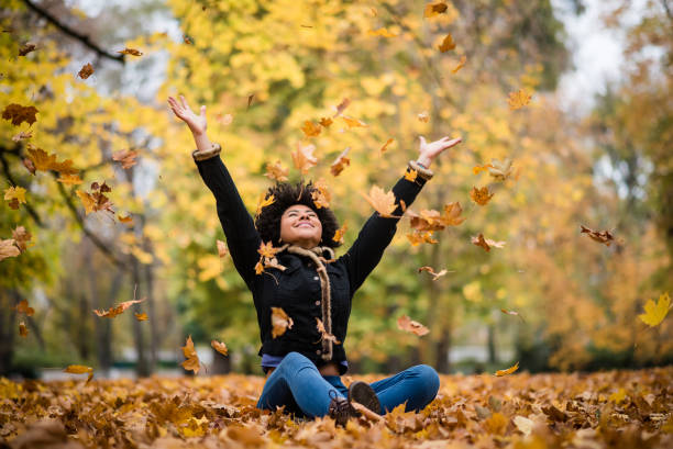 Joyous teen playing with dry maple leaves Happy woman in autumn park drop up leaves arms raised photos stock pictures, royalty-free photos & images