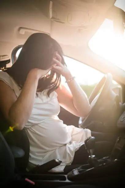 Young depressed pregnant woman behind the steering wheel in car