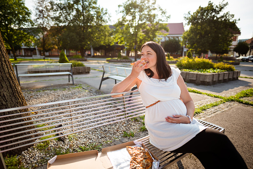 Young pretty pregnant woman eating pizza slice