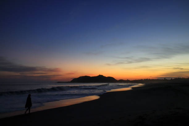 istock Woman Walking on a Pacific Ocean Sandy Beach at Dusk 1016605380