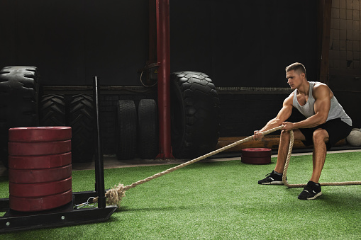 Strong sportsman during his cross training workout. Sled drag exercise.