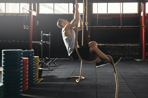 Rope climbing exercise. Sportsman during his cross training workout
