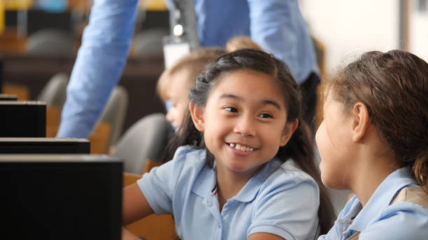 istock Little girl works on computer assignment with friend at school 1016651410