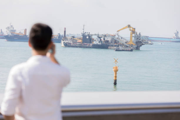 Rear view of mid adult man looking at a ship in a shipping channel in Singapore.