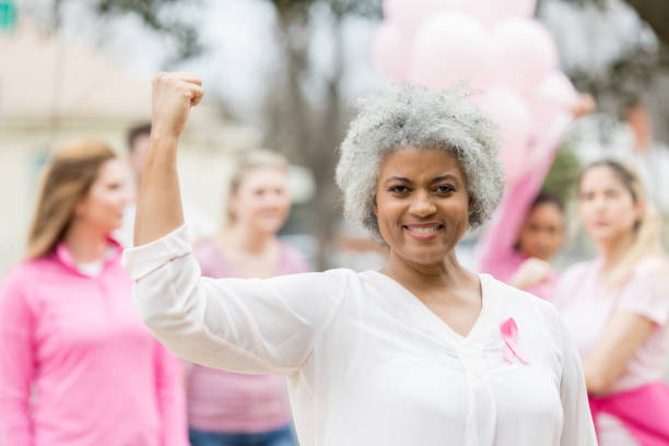 Strong breast cancer survivor flexing muscles Confident senior breast cancer survivor flexes her muscles during breast cancer awareness race. survival stock pictures, royalty-free photos & images