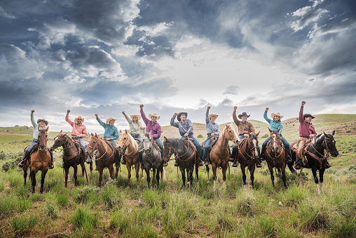 Cowboys and cowgirls cheering, celebrating success. Dramatic sky, fields and Utah mountains