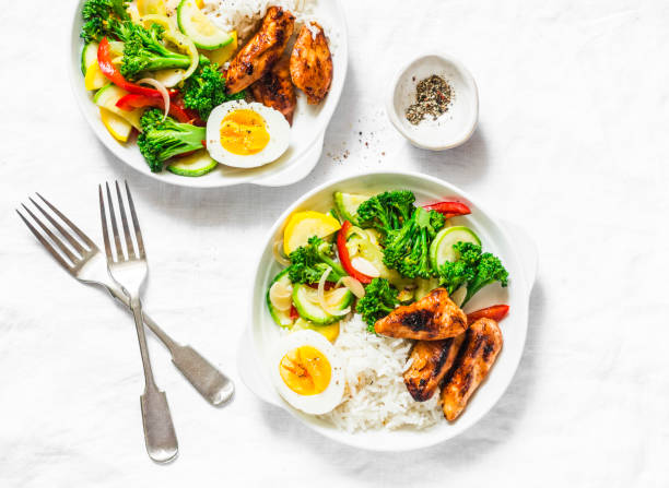 Lunch served - stewed vegetables, rice, boiled egg and teriyaki chicken on light background, top view