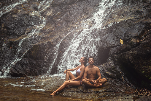 Beautiful young couple is sitting under the cold waterfall during hot day