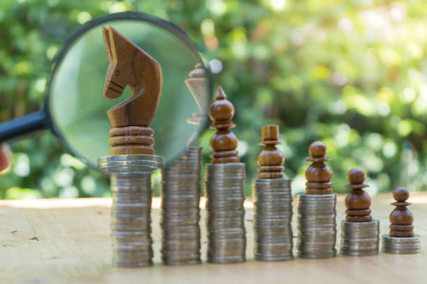 istock Magnifying glass Chess Pieces On Stacked Coins Against green Background 1016737320