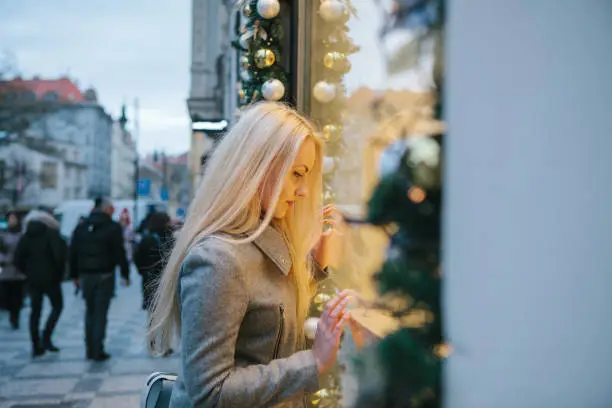 Beautiful young woman next to a shop window in the Christmas holidays. Christmas sales and time to buy gifts or she looks and dreams about the gift.