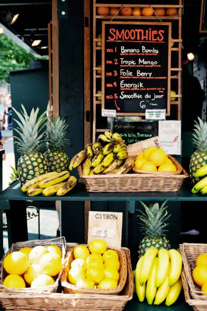 Fruitstand with Bananas, Pineapple and Peaches with a smoothie menu in the blurred background