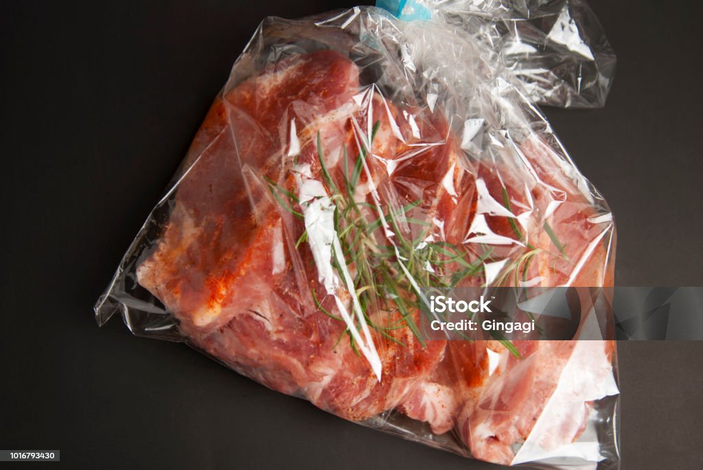 Cooking baking plastic bag. No pastic concept. Fresh pork meat steake packaged in a sleeve with spices, for baking is ready for baking, isolated on black background. Top view. Cooking baking plastic bag. No pastic concept. Fresh pork meat steake packaged in a sleeve with spices, for baking is ready for baking, isolated on black background. Backgrounds Stock Photo