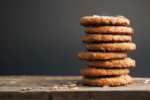 Oatmeal cookies or biscuits with oats, nuts, eggs and flour on brown dark woodenboard with black background, isolated.