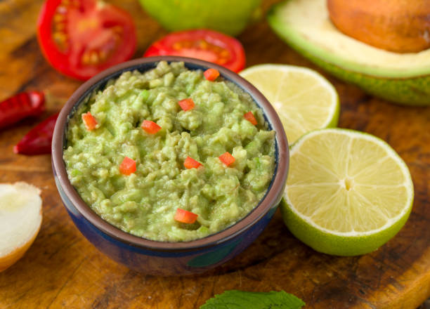 istock Guacamole in blue bowl on natural rustic desk with ingredient: lemon, tomatoes, peppers around. 1016801154
