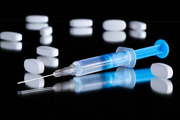 seringue et pilules médicales sur une surface réfléchissante noire - injecting capsule macro pill photos et images de collection