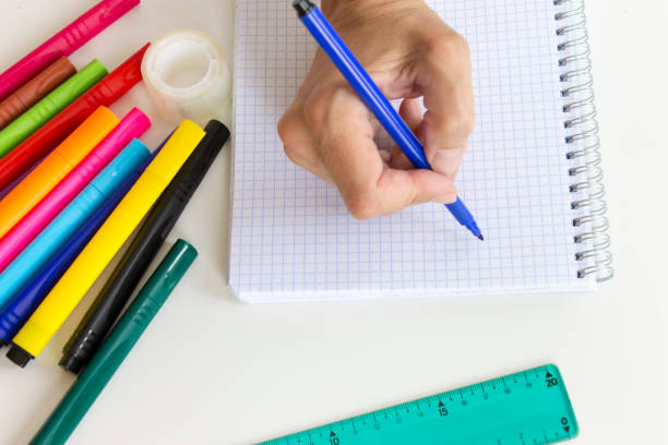 istock Cropped hand writing in notebook. Multicolored marker pens, notebook, ruler on white. Office and school drawing. 1016836842