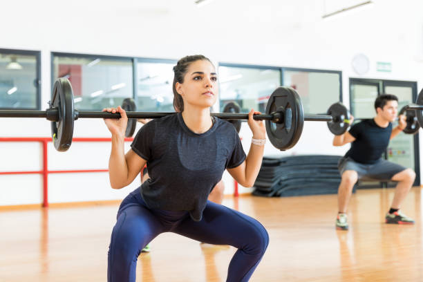 cliente femminile che si allena con il bilanciere nel centro benessere - gym barbell weights exercising foto e immagini stock