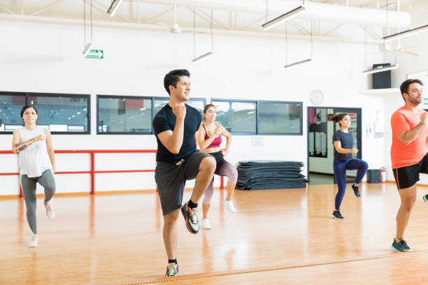 hombre con amigos realizando alta rodilla en clase de aeróbicos - pilates health club gym exercising fotografías e imágenes de stock