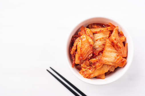 Kimchi cabbage in a bowl with chopsticks on white background, top view, Korean food