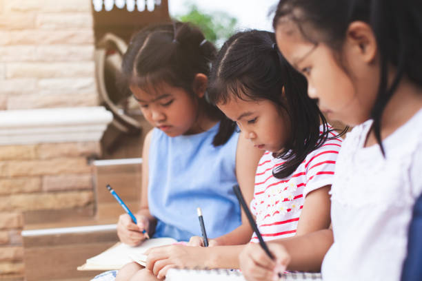 istock Group of asian children reading a book and writing a notebook together 1016971536